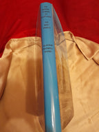 A hardcover book standing upright on a beige satin surface against a red fabric background. The spine is light blue with black text reading 'The Border Towns of Scotland', 'The West March', and 'Alastair Maxwell Irving'.
