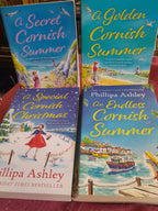 Four books titled 'A Golden Cornish Summer', 'An Endless Cornish Summer', 'A Secret Cornish Summer', and 'A Special Cornish Christmas' by Philippa Ashley on a red surface.