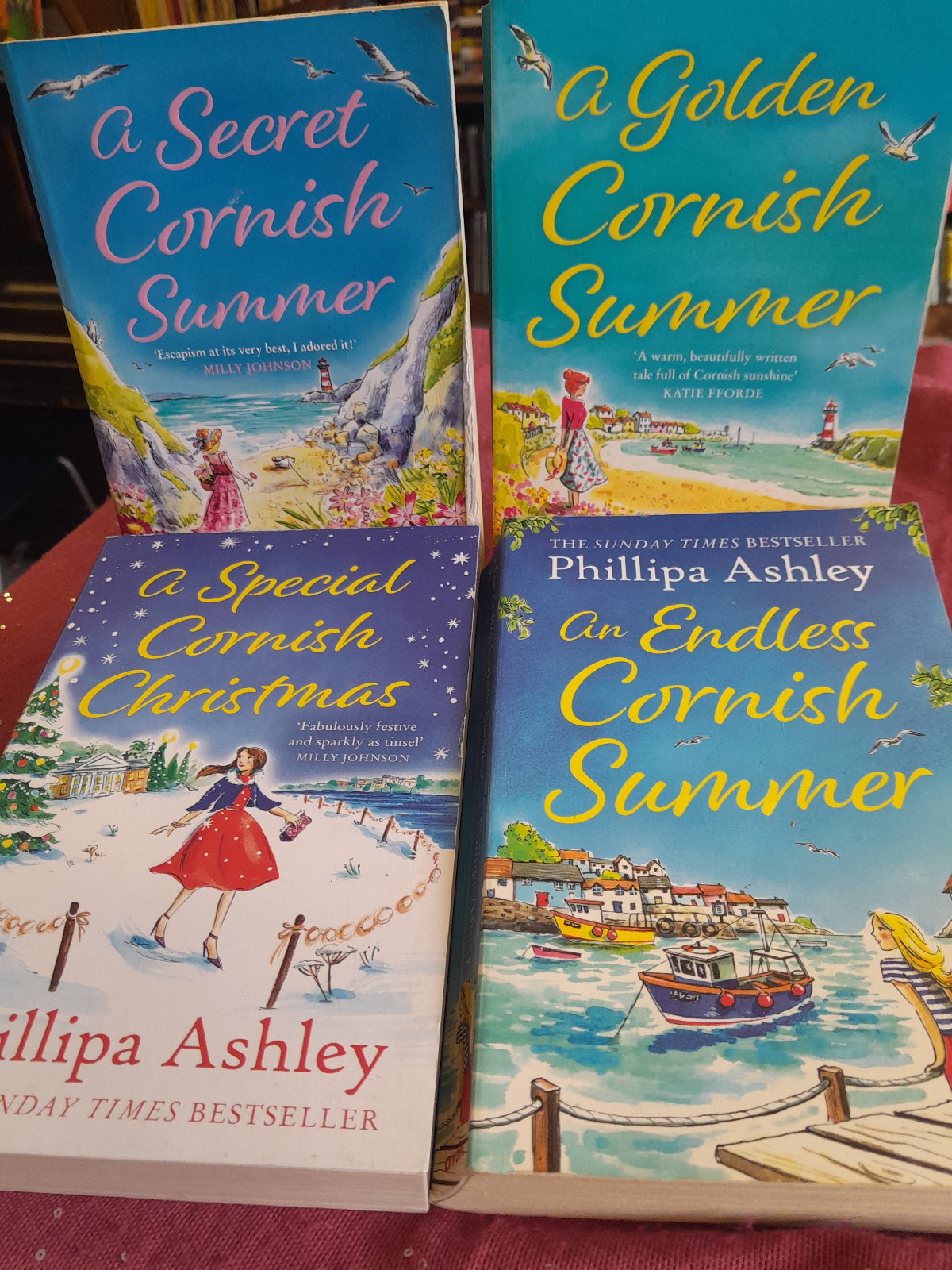 Four books titled 'A Golden Cornish Summer', 'An Endless Cornish Summer', 'A Secret Cornish Summer', and 'A Special Cornish Christmas' by Philippa Ashley on a red surface.