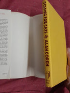 Open book with a yellow cover titled 'Golfing for Cats' by Alan Coren on a red background.