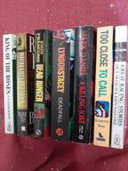 Seven paperback books showing spines on a deep red background
