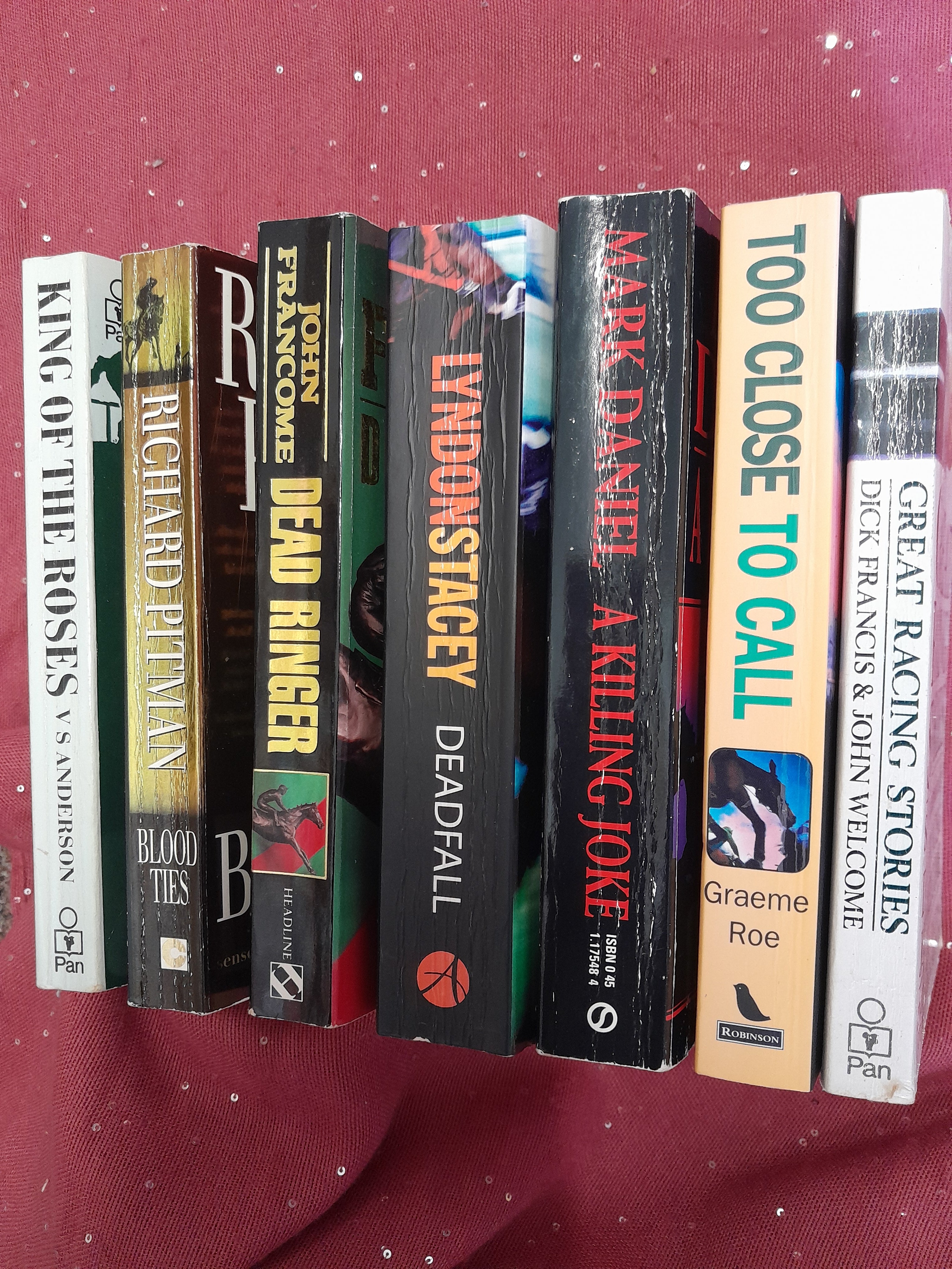 Seven paperback books showing spines on a deep red background
