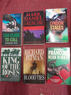 A collection of paperback books laid out on a deep red table cloth, with titles from the horse-racing crime fiction genre.