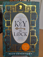 The front cover of the signed copy book 'The Key in the Lock' by Beth Underdown, featuring a dark teal and gold gothic illustration with an orange 'signed copy' sticker.