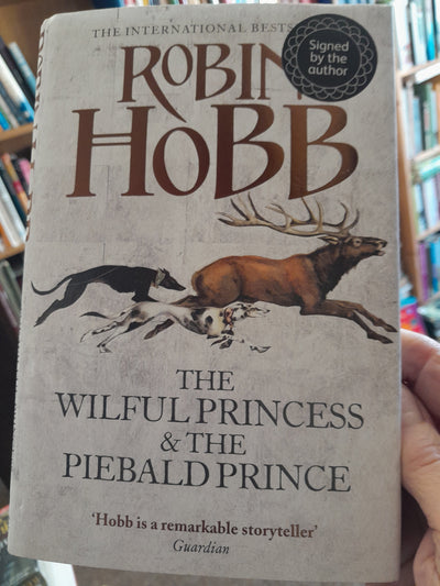 Book titled 'The Wilful Princess & The Piebald Prince' by Robin Hobb held in a hand with blurred background