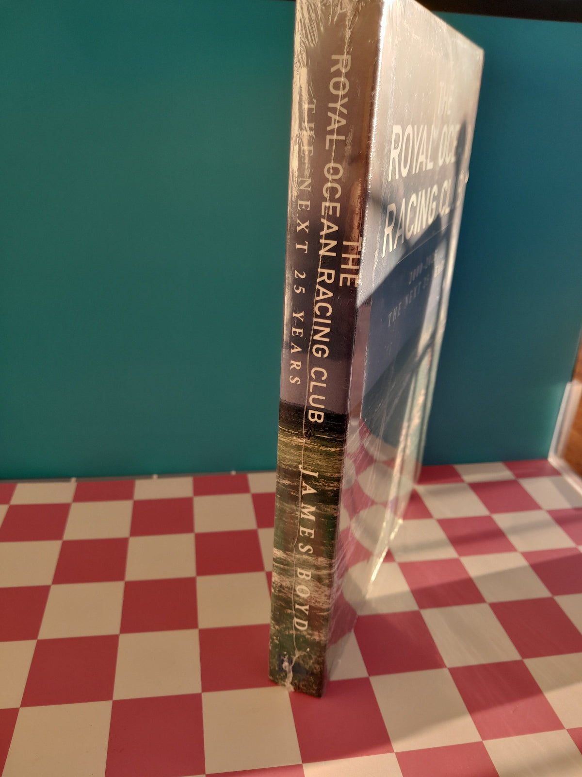 Book titled 'The Royal Ocean Racing Club: The Next 25 Years' by James Boyd on a checkered surface.