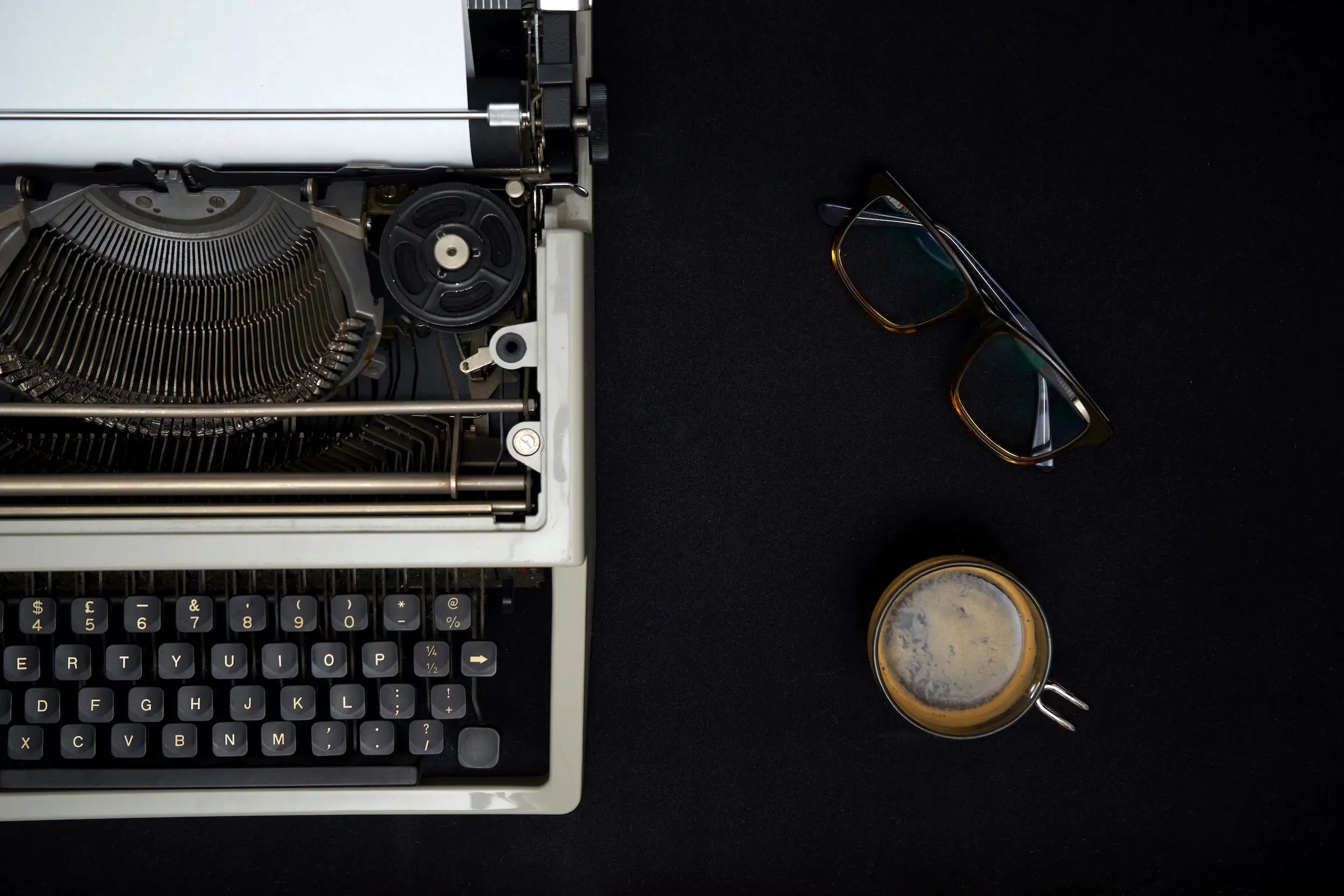 Vintage typewriter on a dark surface with a cup of coffee and glasses.